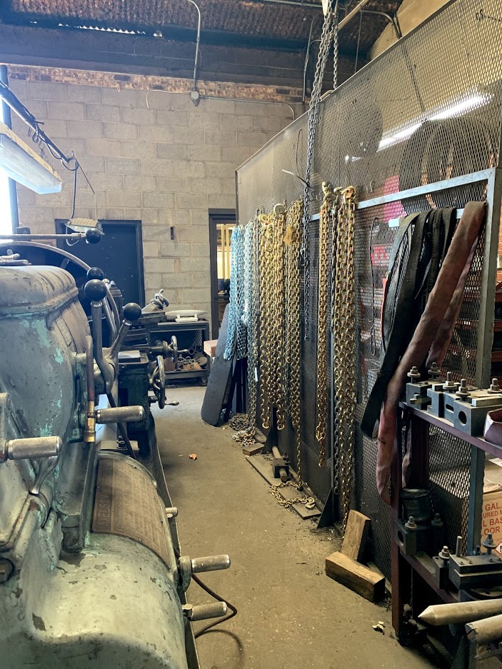 Heavy-duty tow and logging chains hanging on a wall rack inside Riggs Machine & Welding supply area, Stephenville, TX