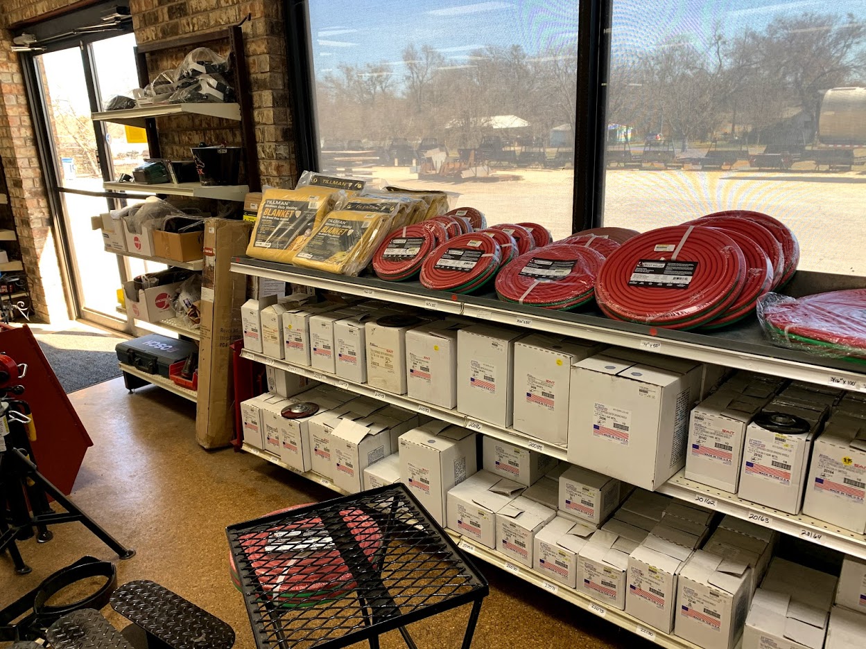 Shelf of Tillman welding blankets and coiled red oxy-acetylene hose at Riggs Machine & Welding supply store in Stephenville, TX, with boxed SAIT abrasives below